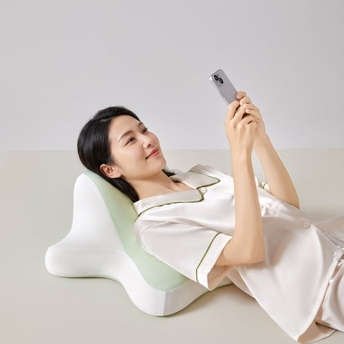 グリーンのマルチピローに頭と背中をあずけて、スマホを見る女性